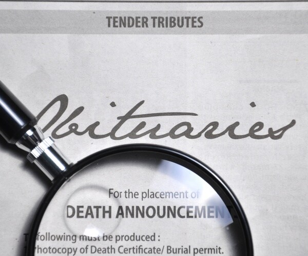 magnifying glass on newspaper obituary page