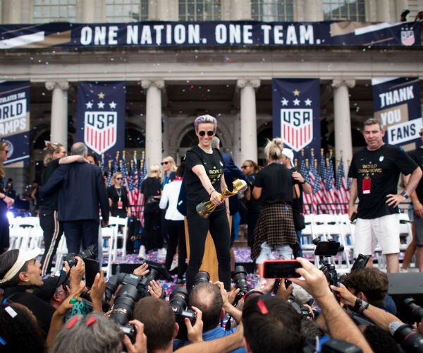 megan rapinoe holds the trophy as fans reach toward her