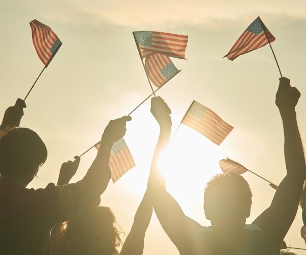 people waving american flags with the sun in the background