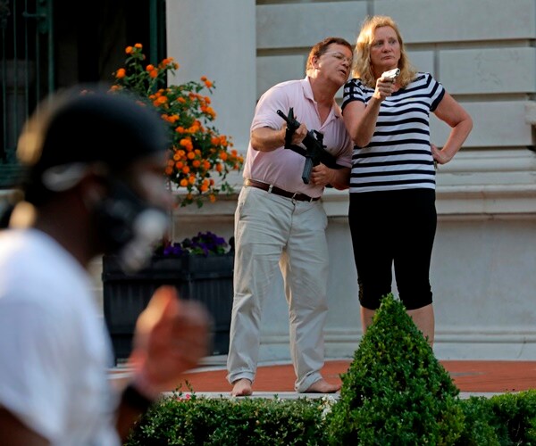 mark and patricia mccloskey stand outside their home holding guns while protestester walk by