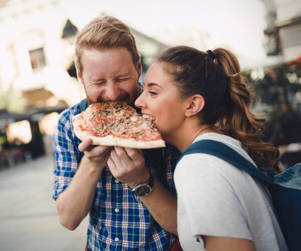 man and woman on street eating pizza