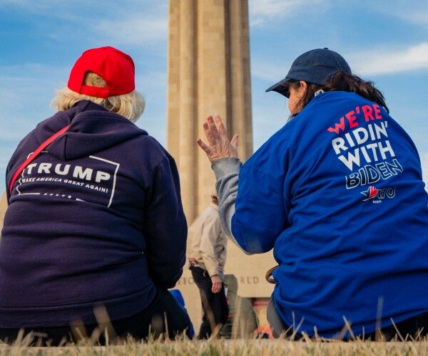 a trump supporter wearing a red hat and trump hoodie talks to a biden supporter wearing a tshirt