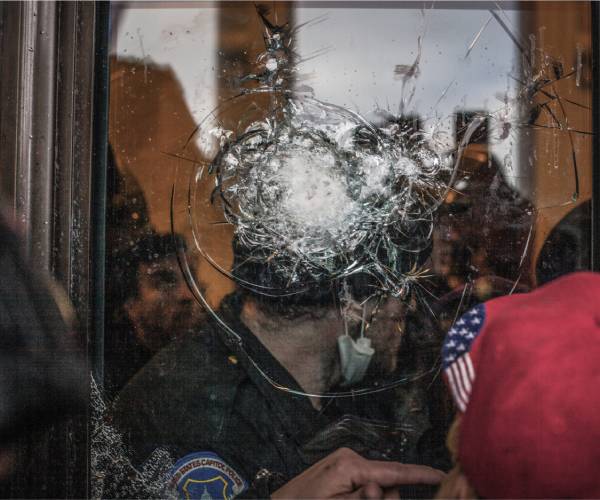 police officer behind a shattered window with protesters outside