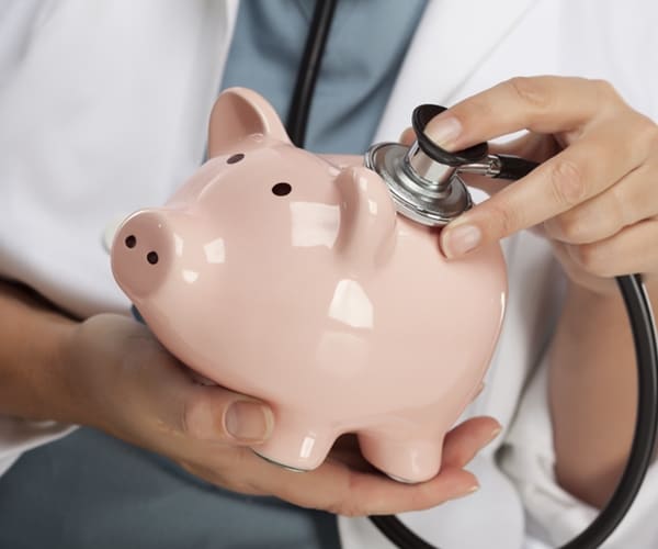 doctor holding stethoscope to pink piggy bank

