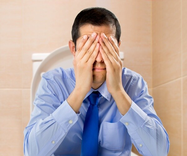 man sitting on toilet with head in hands