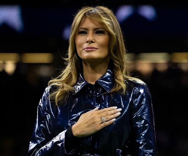 melania trump wears a black raincoat and has her hand over her heart