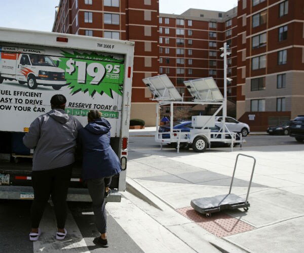 two college students load items in a uhaul truck with the dormitory in the background