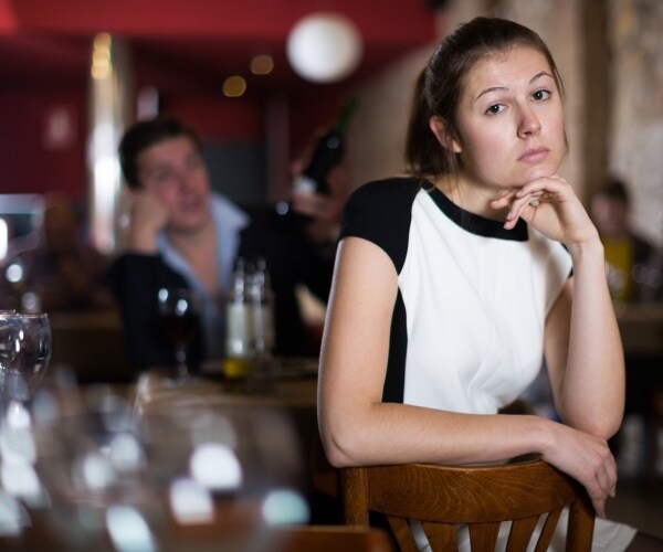 woman looking sad because her friend is drinking too much at bar