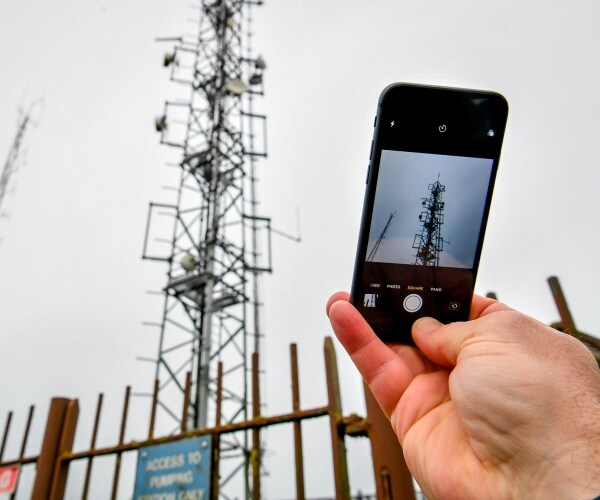 person takes a picture on an iphone of cell towers