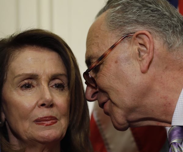 close-up of senator chuck schumer turning to his right to speak into representative nancy pelosi's left ear