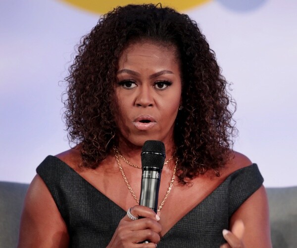 michelle obama in a black dress speaking on stage into a mic