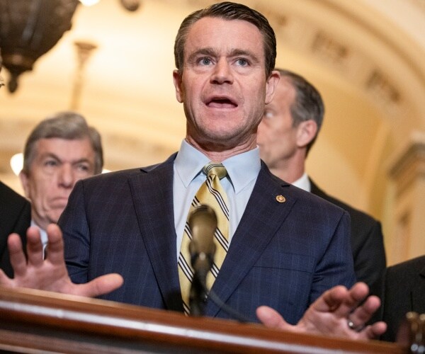 todd young stands at a podium speaking with gop leaders behind him.