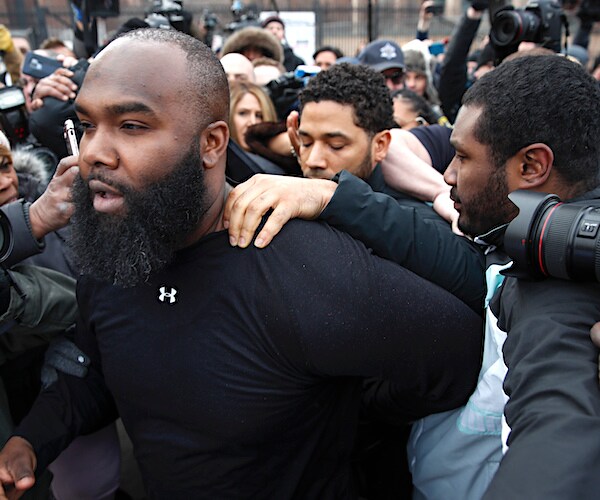 actor jussie smollett is hounded by throngs of people and is led by another hulking man as he leaves jail