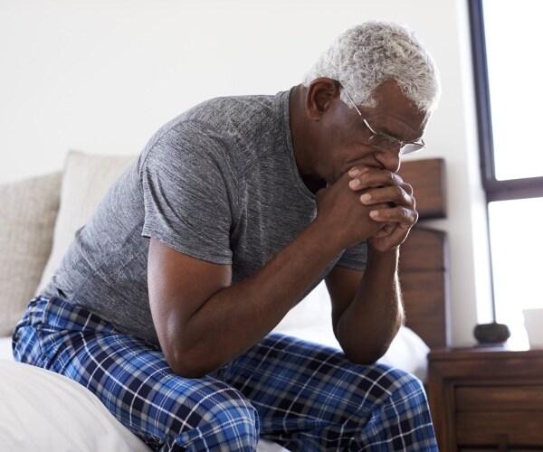 man sitting on edge of bed looking depressed