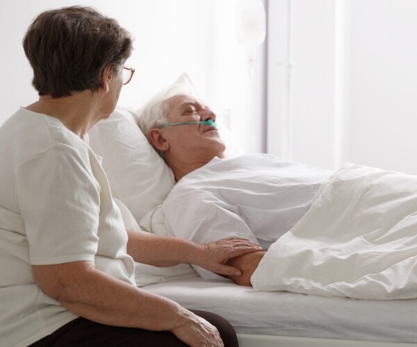 a woman sits by the bed of a man in a coma