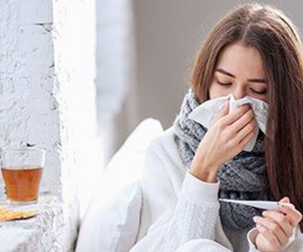 woman blowing nose, taking temperature, tea on table