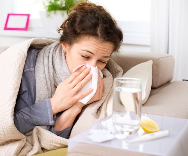 woman sick with flu, blowing nose, tissues on table, tea, thermometer