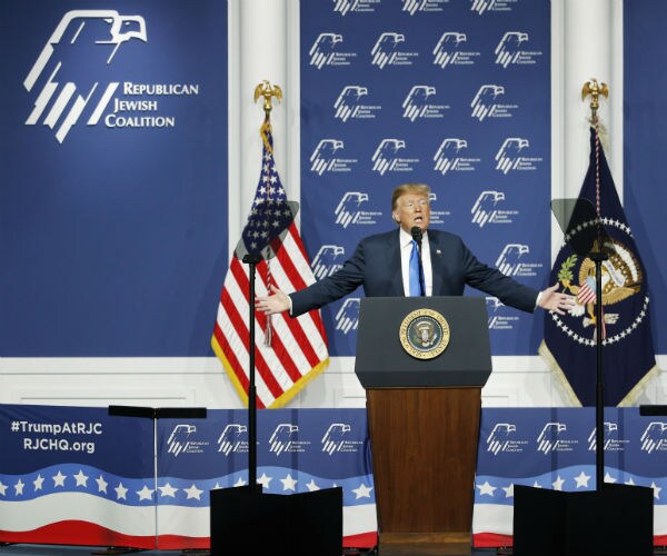 president donald trump speaks at the republican jewish coalition with the logo in the background and flags on stage