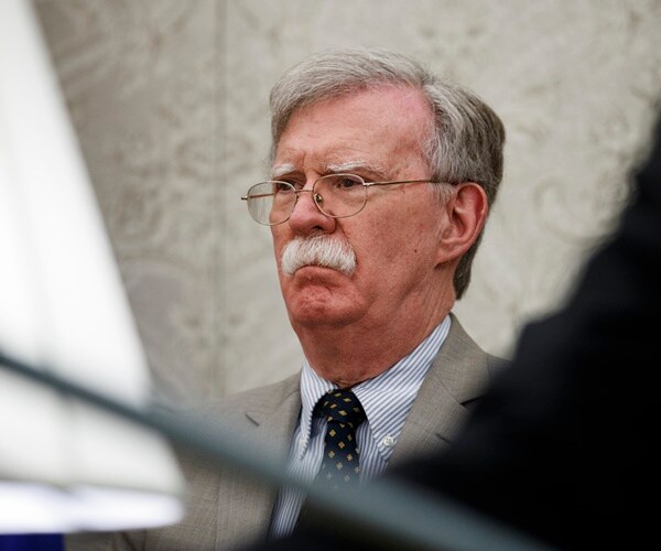 john bolton listens to a speaker
