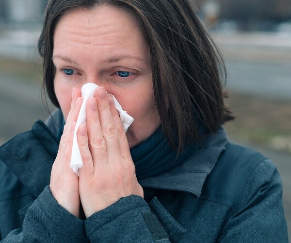 woman blowing her nose stands outside