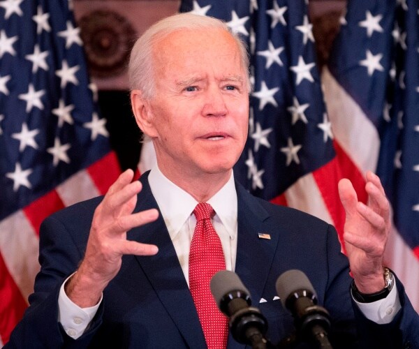 biden in a suit and red tie with us flags behind him