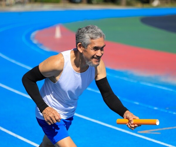 older man running on a track with a baton in his hand