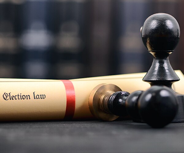 a photo illustration of a scroll reading election law and a pair of black pawns on a brown table