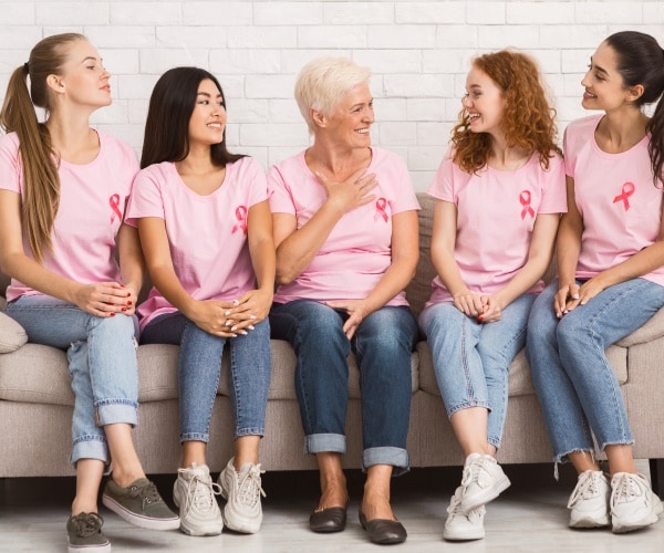 women sitting on a couch wearing pink t-shirts and pink breast cancer ribbon