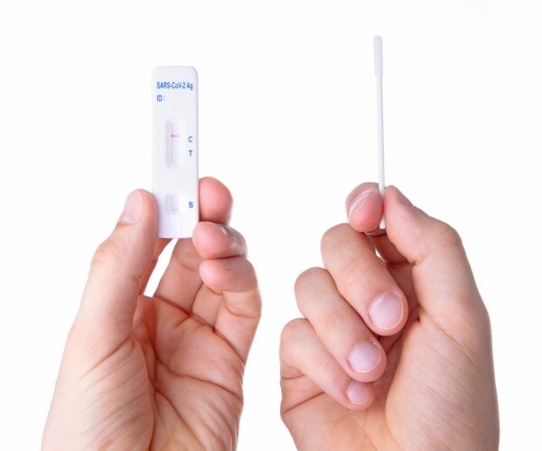 One hand holds rapid antigen COVID test and the other a swab