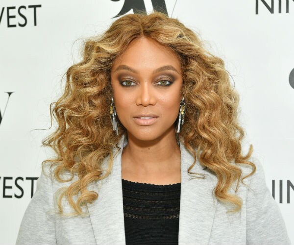 tyra banks is seen with blonde hair, sparkling earrings, gray jacket and black camisole 