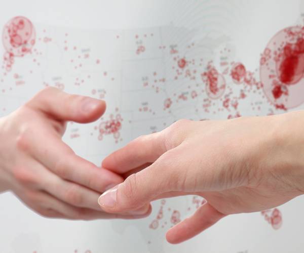 hands reaching out to each other in front of a map showing coronarvirus cases