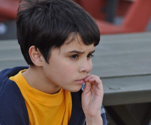 young boy biting fingernail and looking scared