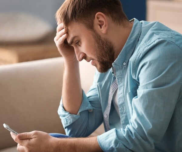 man holding head, depressed, holding cellphone in hand