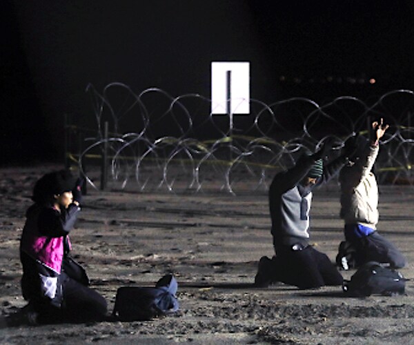 honduran migrants kneel and hold up their hands after walking onto united states territory from tijuana, mexico