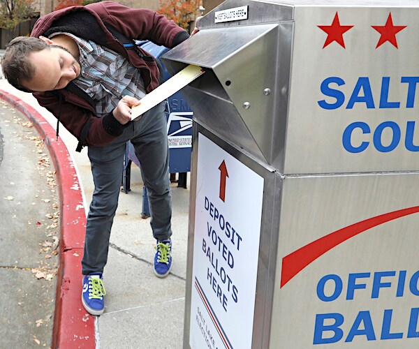 a man puts a voting ballot into a public ballot box