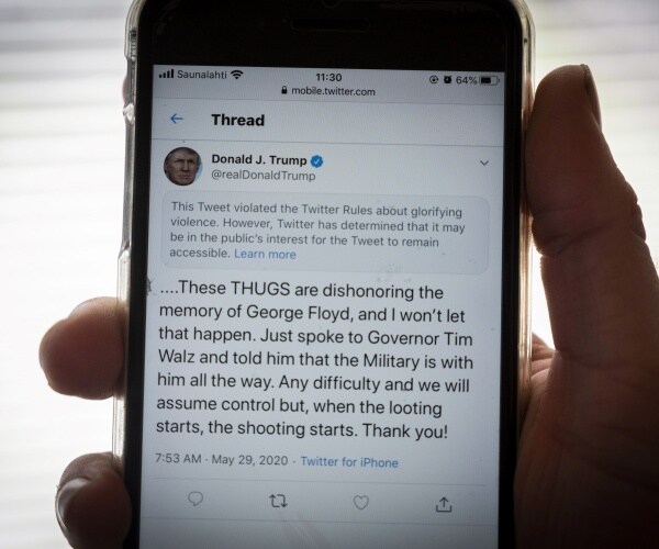 hand holding iphone displaying trump tweet with label added by twitter above saying trump glorified violence