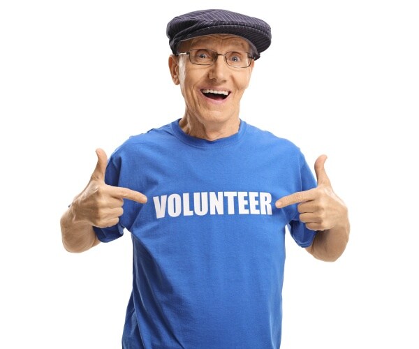 older man smiling and wearing and pointing to his t-shirt that says 'volunteer'