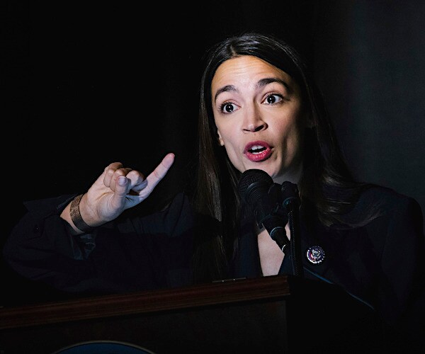 alexandria ocasio-cortez exults during a campaign speech on a dark stage