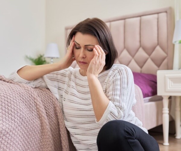 woman sitting on floor next to bed looking depressed