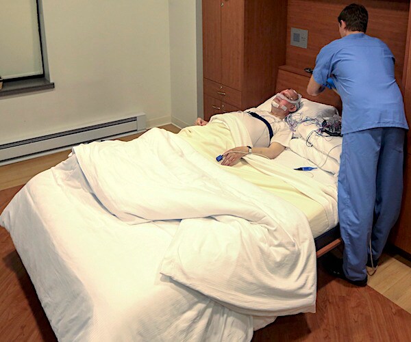 a senior gets set up for a sleep test on a bed in a hospital room