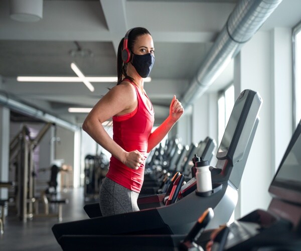 woman wearing mask running on a treadmill in a gym 