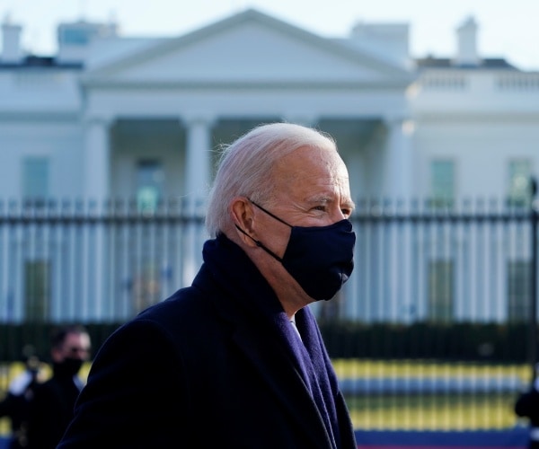 biden in a black face mask standing outside the white house