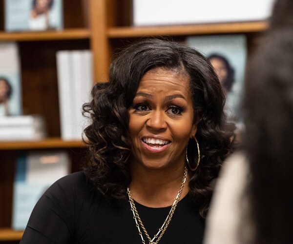 michelle obama smiles while sitting at a table