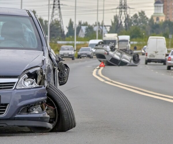 car crash is shown with headlights blown out and tires broken and car flipped over in the background