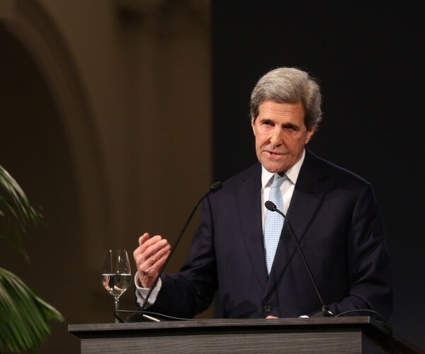 john kerry in a black suit and light blue tie speaking at a podium 