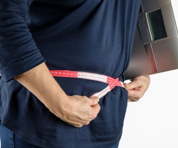 overweight person with measuring tape around waist, holding a scale