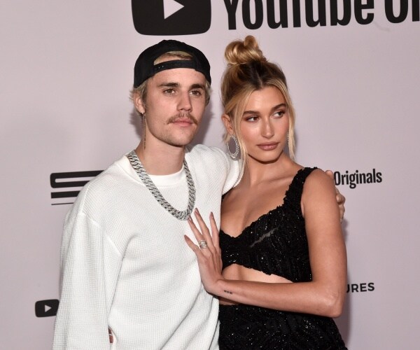 justin bieber in a white long sleeve shirt and black cap with hailey in a black cut out dress