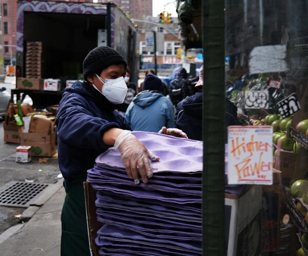 man wearing a face mask empties vegetables at a market in nyc chinatown