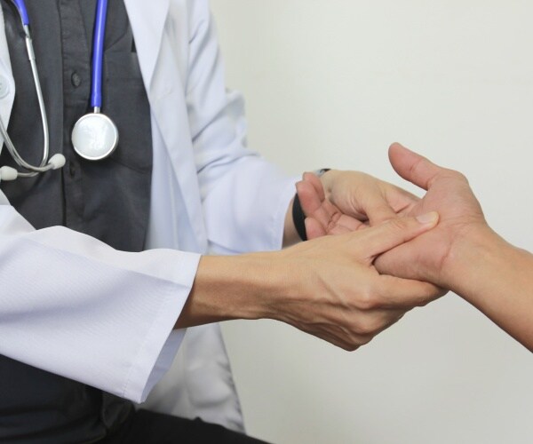 physician examines hand of patient with Parkinson's