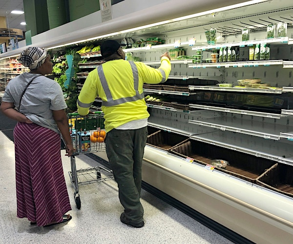 Shoppers walk near empty shelves of produce at a Publix Supermarket on Tuesday in Miami Shores